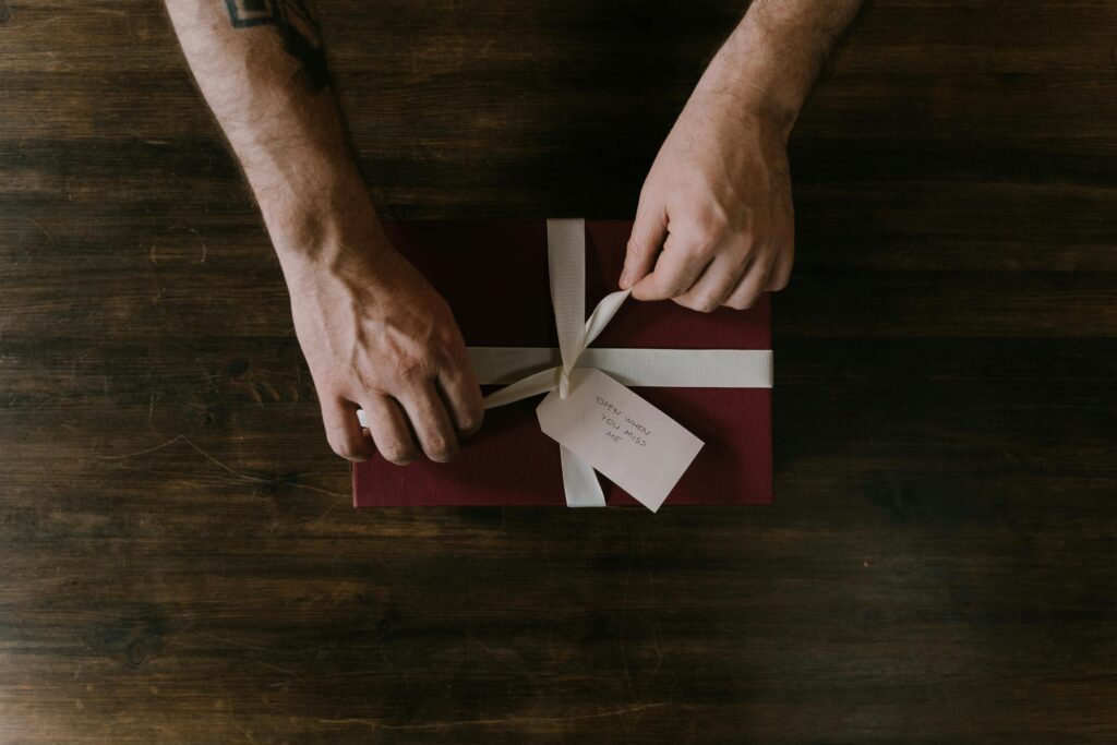 Hands wrapping a red gift box with a white ribbon on a wooden surface, ideal for holiday or celebration themes.